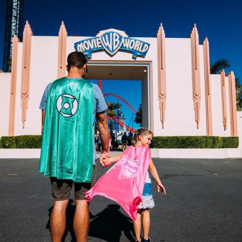 gc-tourism-father-in-green-superhero-cape-holding-hand-of-daughter-in-pink-supergirl-costume-movie-world-entrance