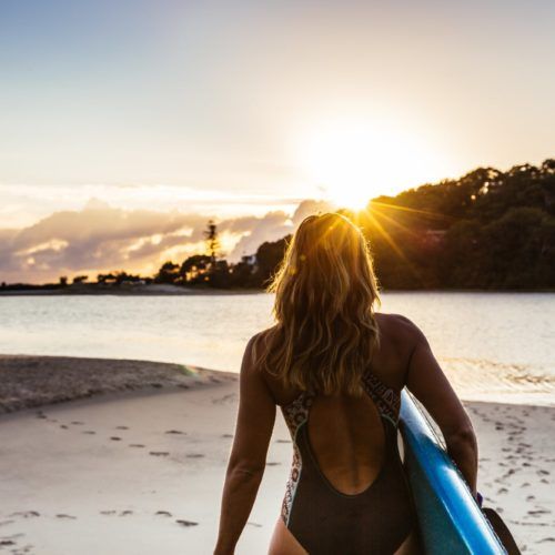 girl-walking-along-beach-with-paddleboard-at-sunrise-at-currumbin-creek